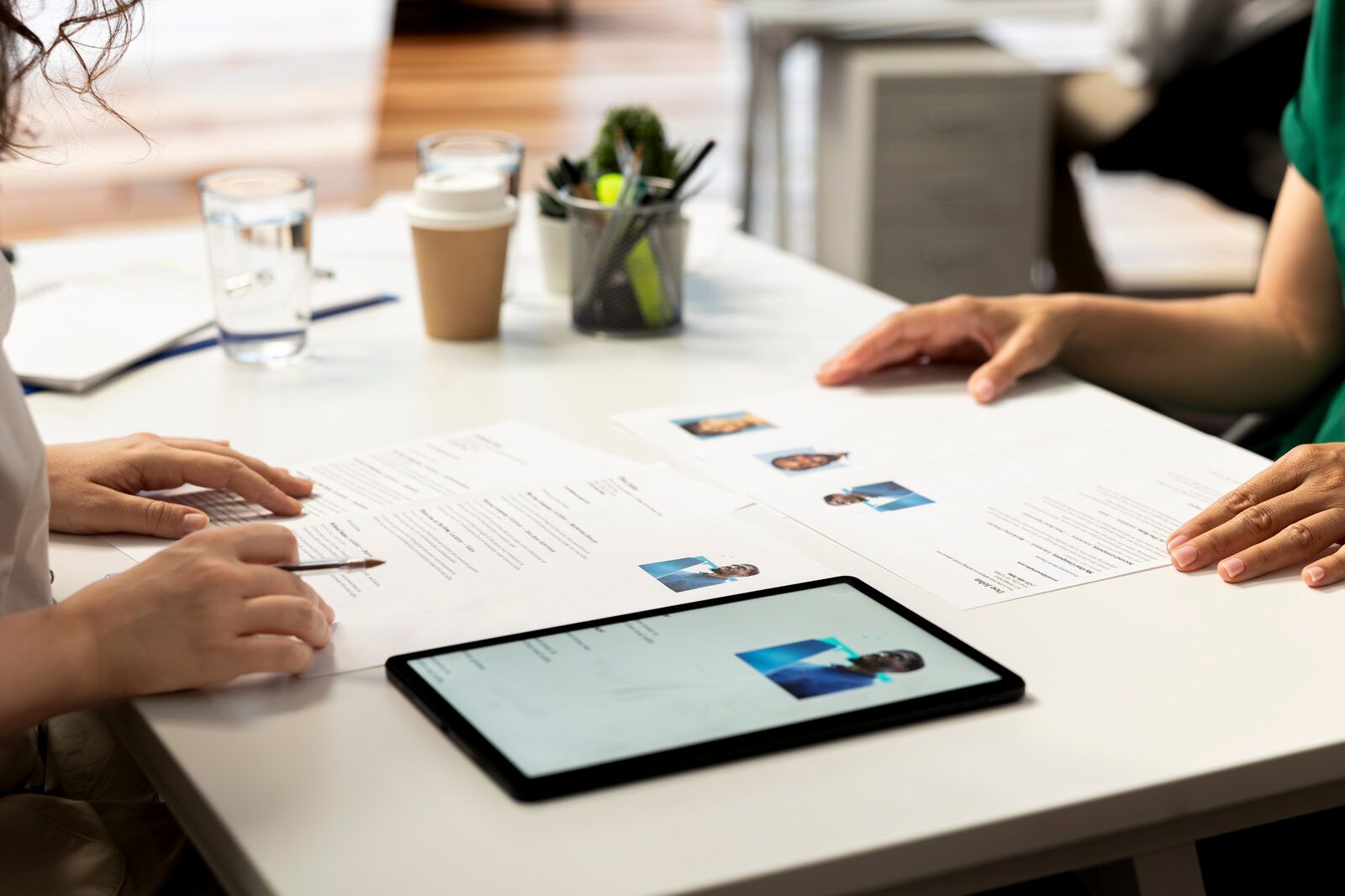 Two colleagues reviewing CVs at a white meeting table, a tablet and notes in front of them
