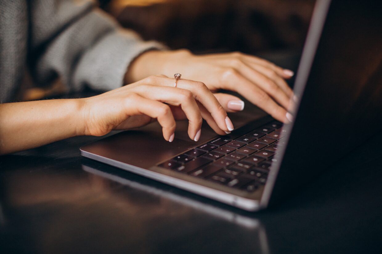 A hand typing on a laptop keyboard, close up, on a dark desktop