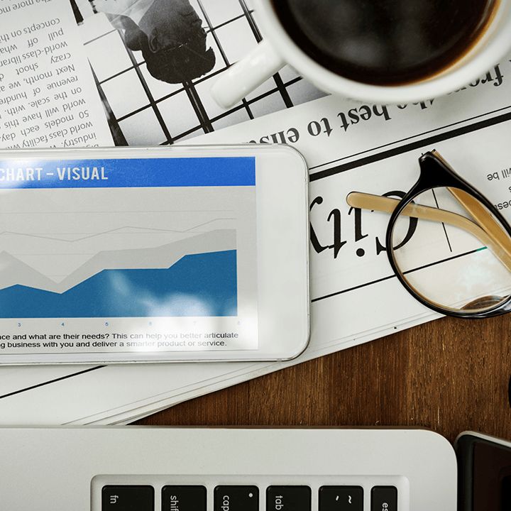 Share price chart on a tablet resting on a financial daily, beside glasses and a cup of coffee