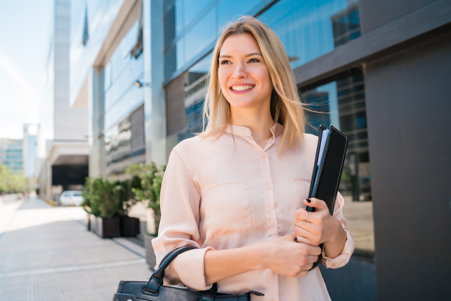 A smiling colleague holding documents in front of an office building
